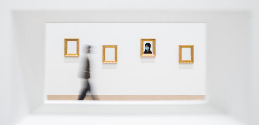 The view from peering into a porthole of an installation: from the other side, another viewer peers through a porthole on the other side, their visage framed by a golden frame