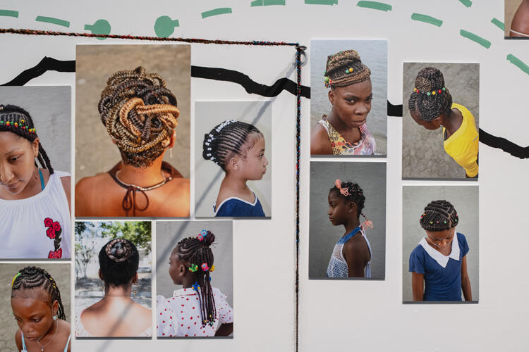 Installation view of a white wall with images of the hair and sometimes faces of a number of dark-skinned people connected by various lines