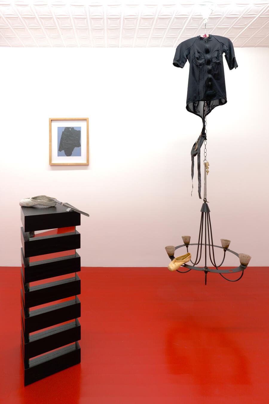 A black shelf with a ballet shoe and butter knife balanced atop; a chandelier made mostly with ballet-related ephemera, bandages framed in background