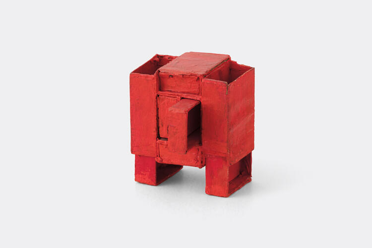 An image of a blocky red sculpture with rugged edges, certain aspects coming foward or backward, in the vague shape of a stocky human