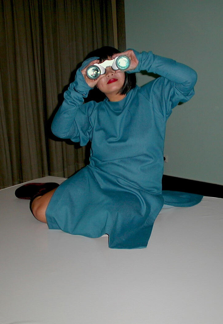 An asian woman in teal dress holding binoculars up to her eyes