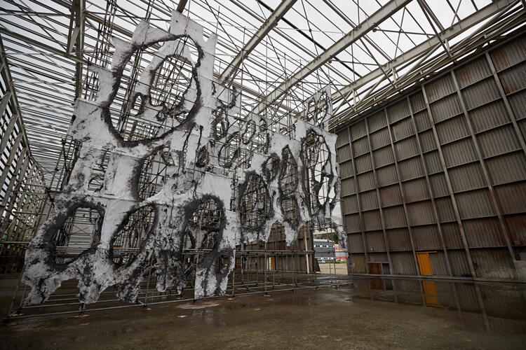 A large-scale many-holed fabric sculpture set against scaffolding