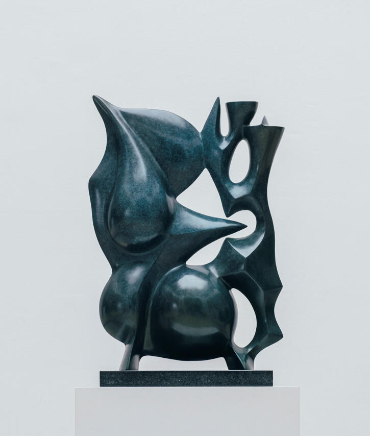 A dark blue/ teal sculpture that looks vaguely like a powerful insect curled up: round and sharp parts to the sculpture