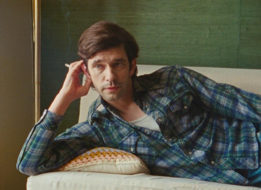 Ben Whishaw as Peter Hujar holds cigarette and hand to head while laying on side