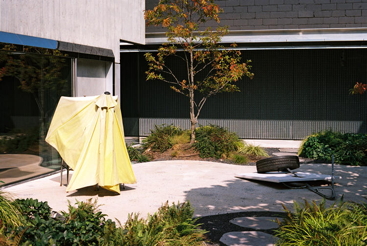 Outside, in a Brooklyn courtyard: a half-open yellow umbrella that looks almost like a ghost, a tire attached to a piece of board